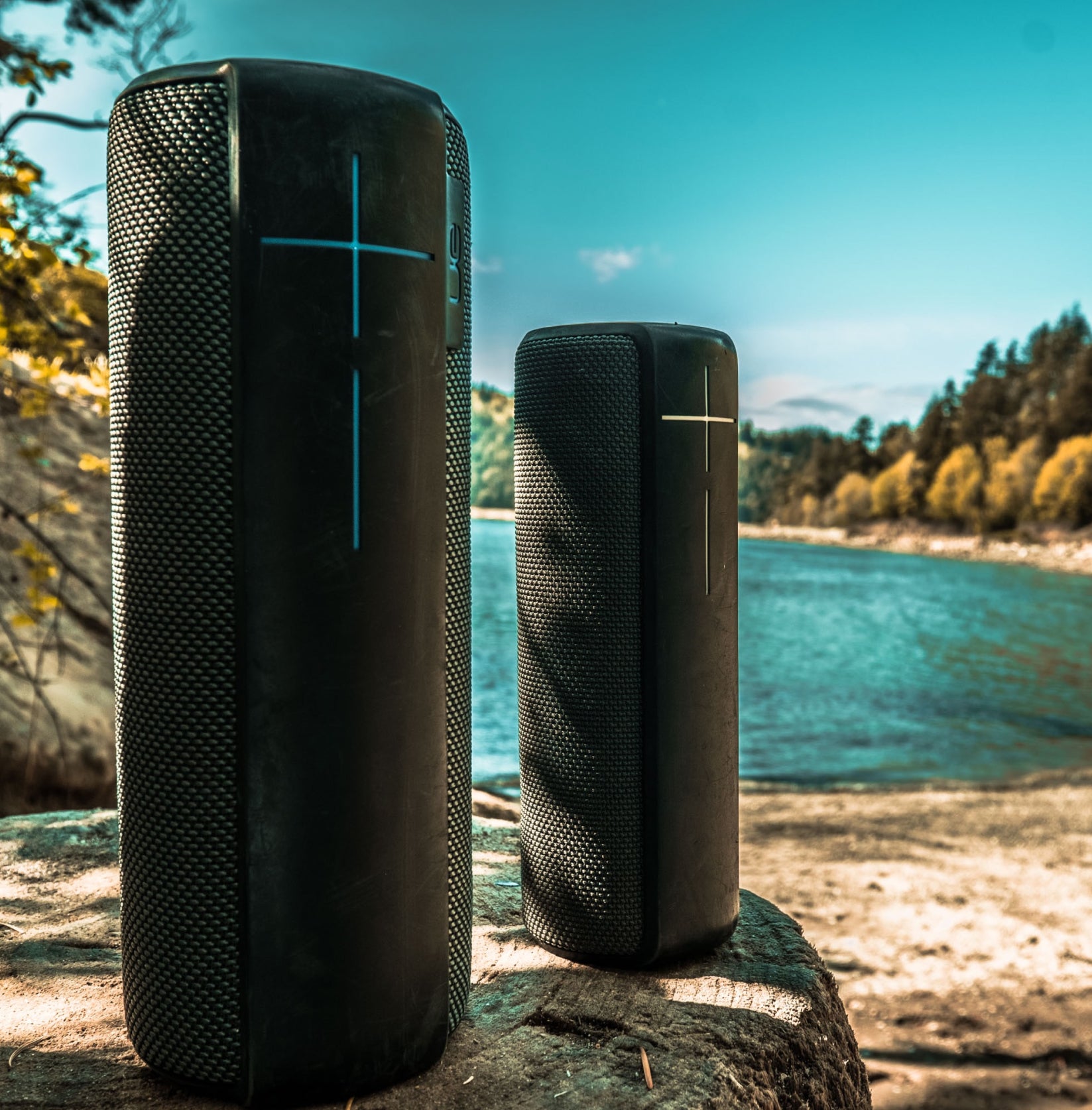 Two black wireless speakers outside, near a remote lake